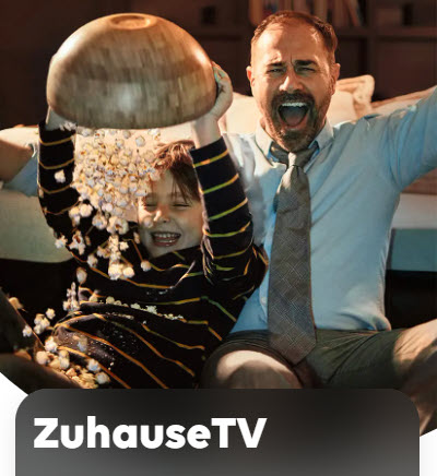 Mann und Junge jubeln auf dem Sofa. Der Junge überschüttet sich vor Freude mit dem Popcorn.